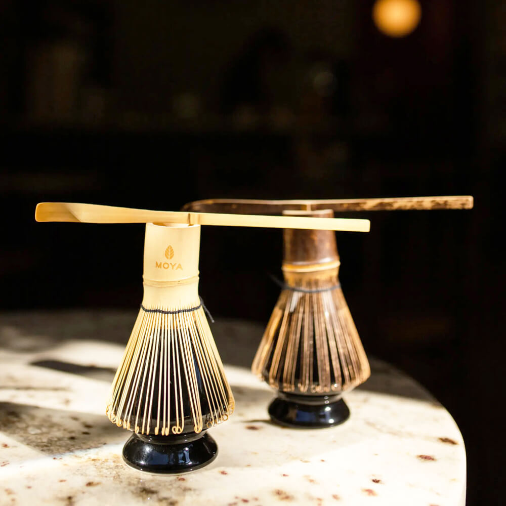 Világos bambusz matcha teakanál bambusz habverőn, sötét háttérrel és hangulatos lifestyle beállításban.