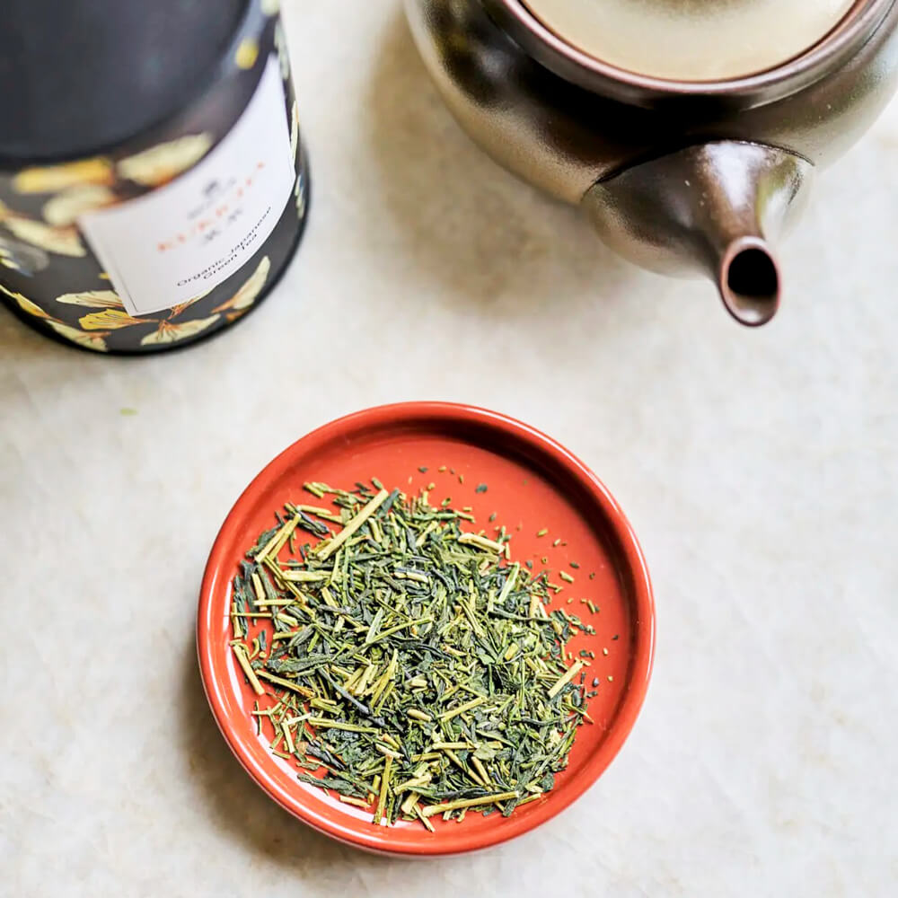 Moya Kukicha organikus japán zöld tea levelei piros tálkában, teáskannával felülnézetből