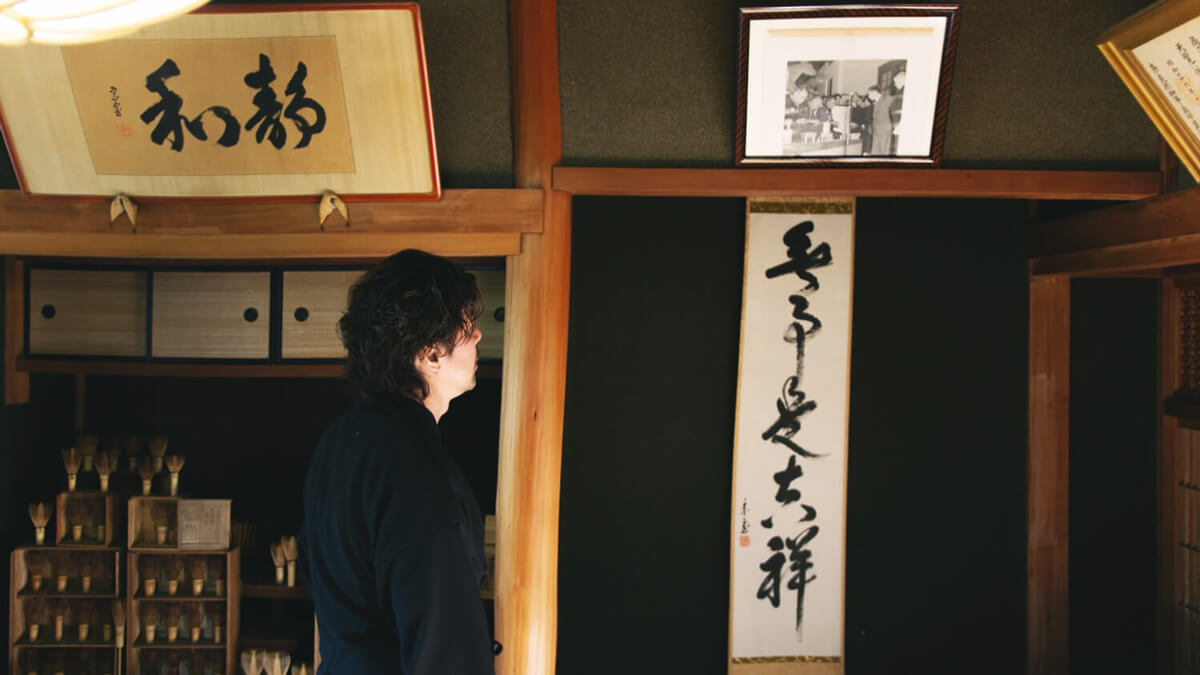 Chasen készítő mester a műhelyében Japán mester a chasenekkel teli polcok mellett, kalligráfiák között