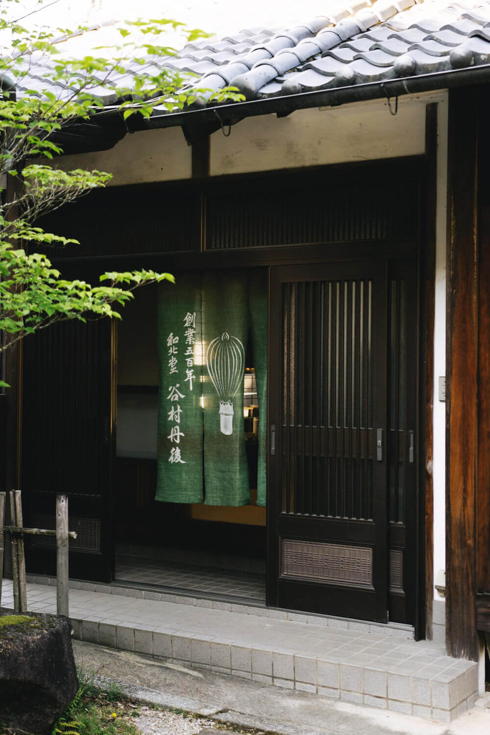 Chasen készítő műhely bejárata bambusz ecset Hagyományos japán műhely bejárata zöld noren függönnyel és chasen (bambusz ecset) motívummal