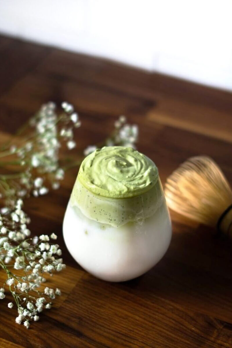 Dalgona Matcha réteges pohárban, zöld habbal a hideg tej tetején.