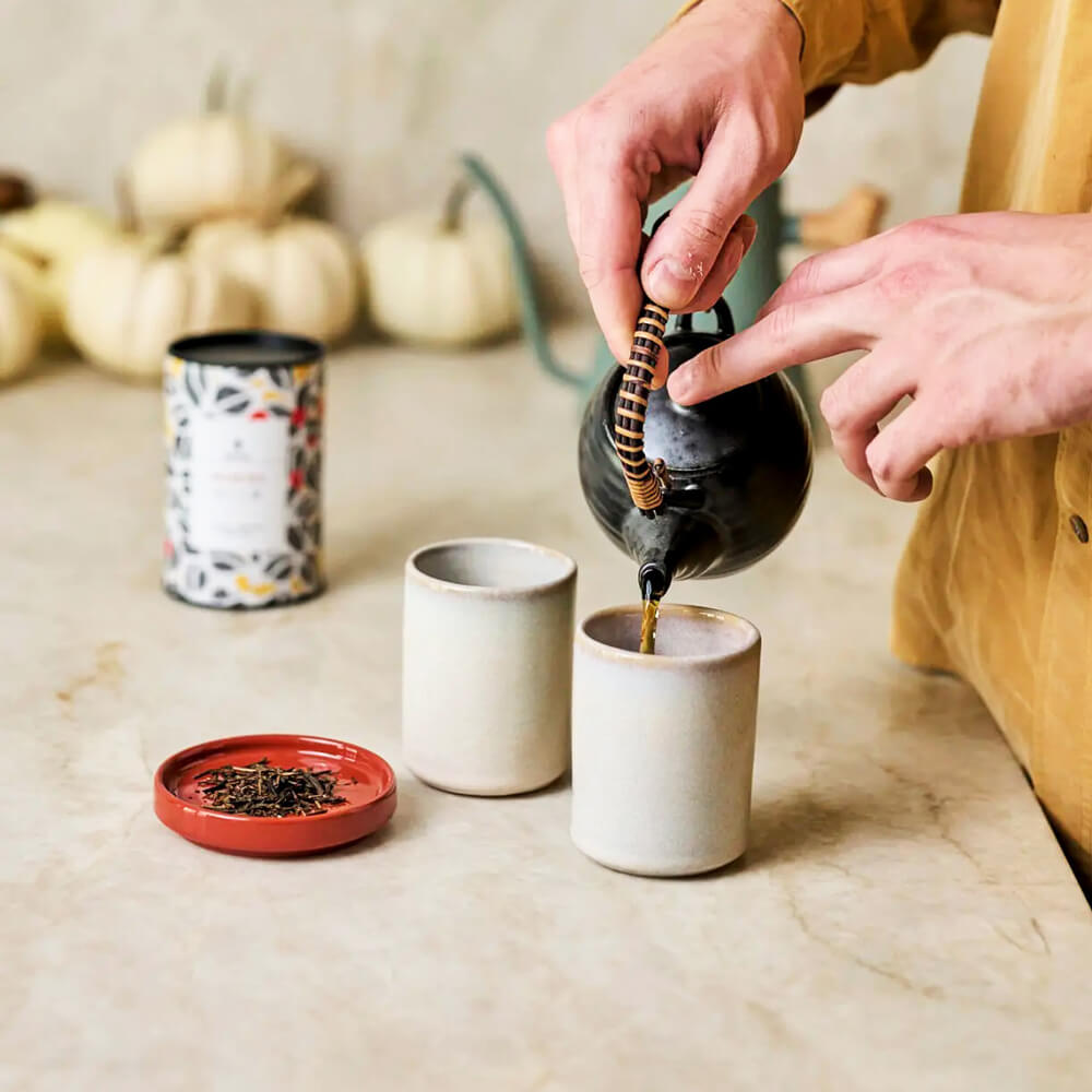 Josei Kerámia Teásbögre két bögrével a pulton, teát töltenek az egyik bögrébe, mellette tealevél tálkán
