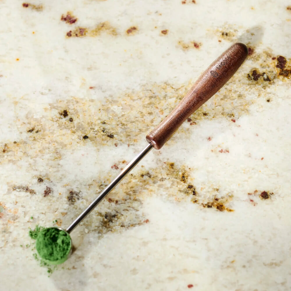 Matcha Adagolókanál közelről: fa nyél és fém kanál matcha porral márvány felületen