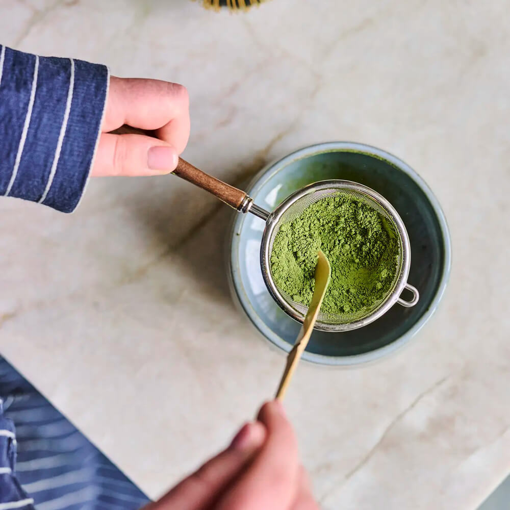 Matcha Szűrő és Szita felülnézetből: matcha por a fém szitában, kerámia tál fölött