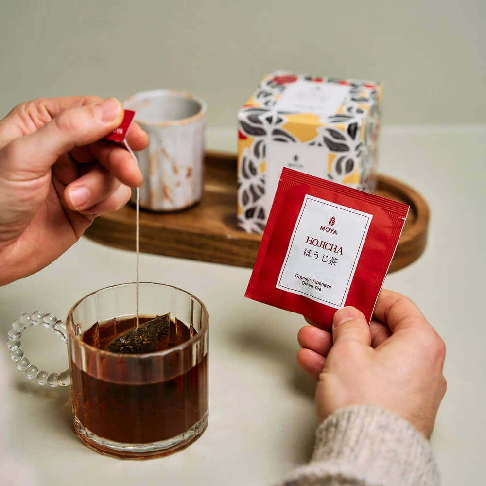 MOYA Hojicha organikus japán filteres zöld tea tasak és tea üvegcsészében, dobozzal a háttérben