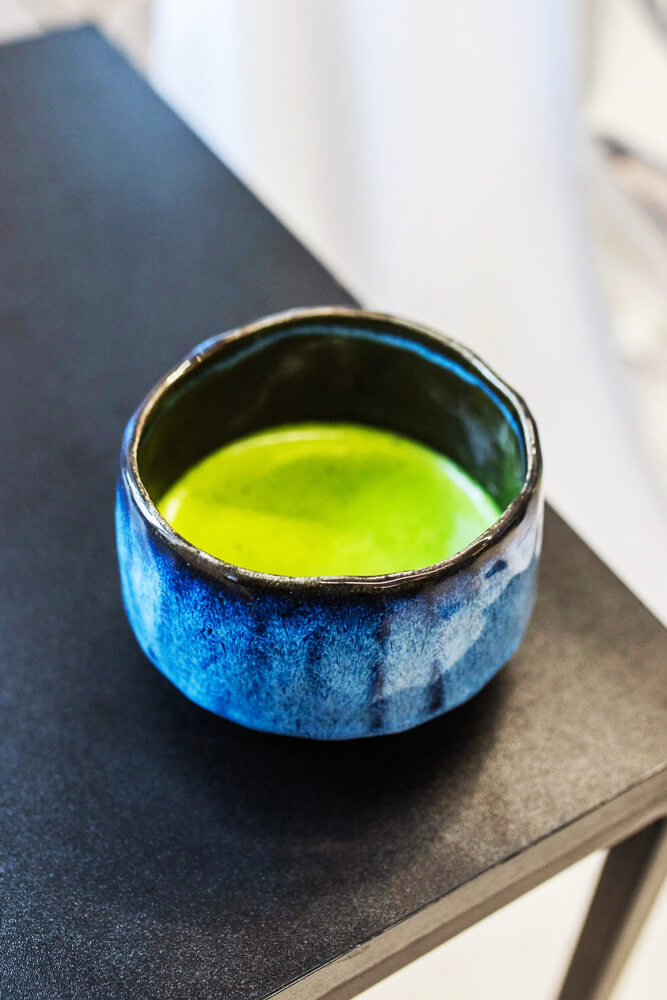 Japán Kerámia Matcha Tál - Taro kék kerámia tálban elkészített matchával, közeli nézetben fekete felületen