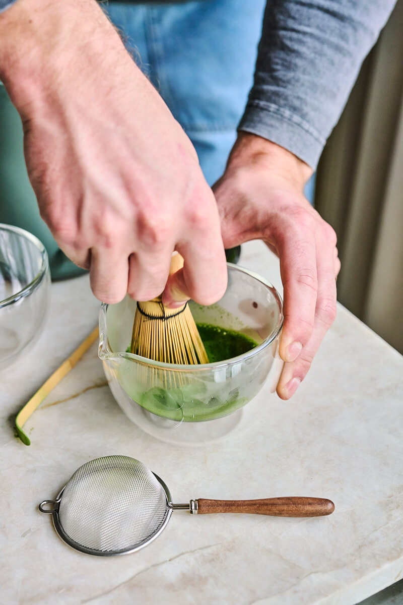 Kéz bambusz chasen habverővel habosítja a matcha teát egy kerámia tálban