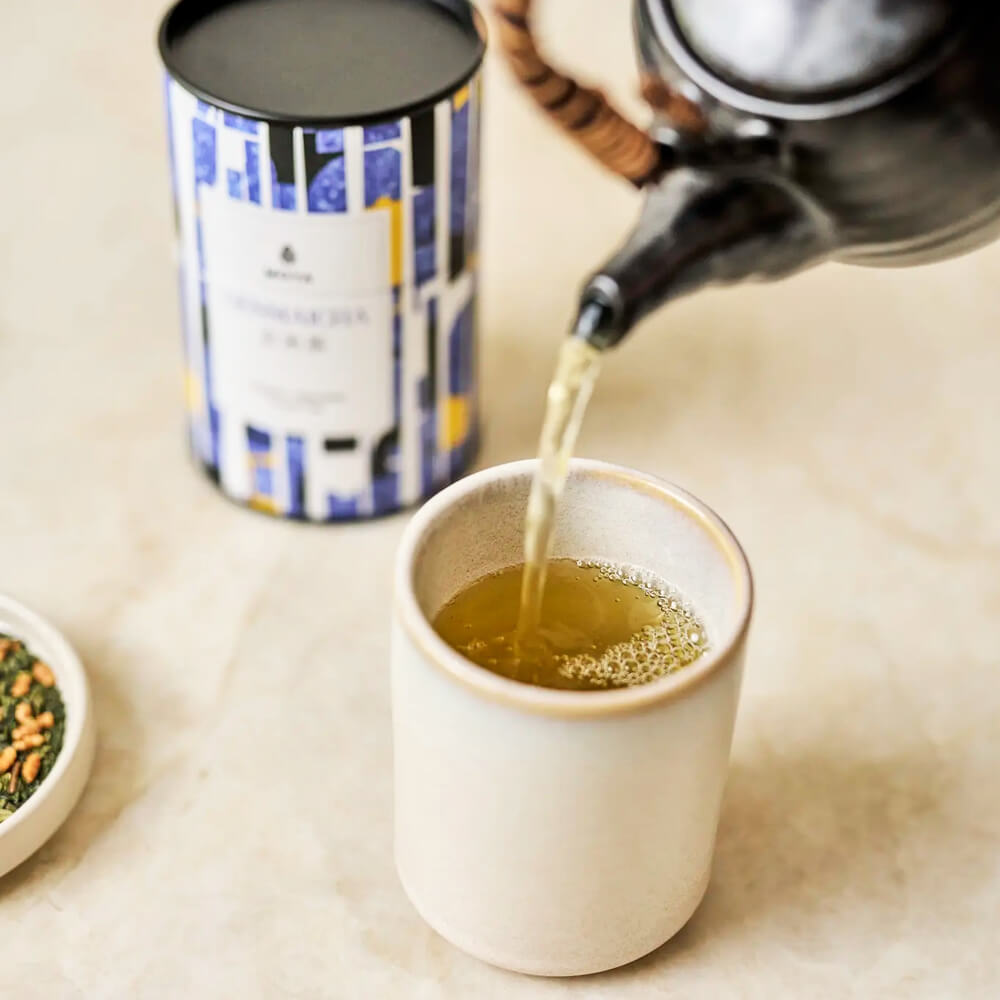 Moya Genmaicha organikus japán zöld tea kitöltése bögrébe teáskannából, a doboz a háttérben látszik