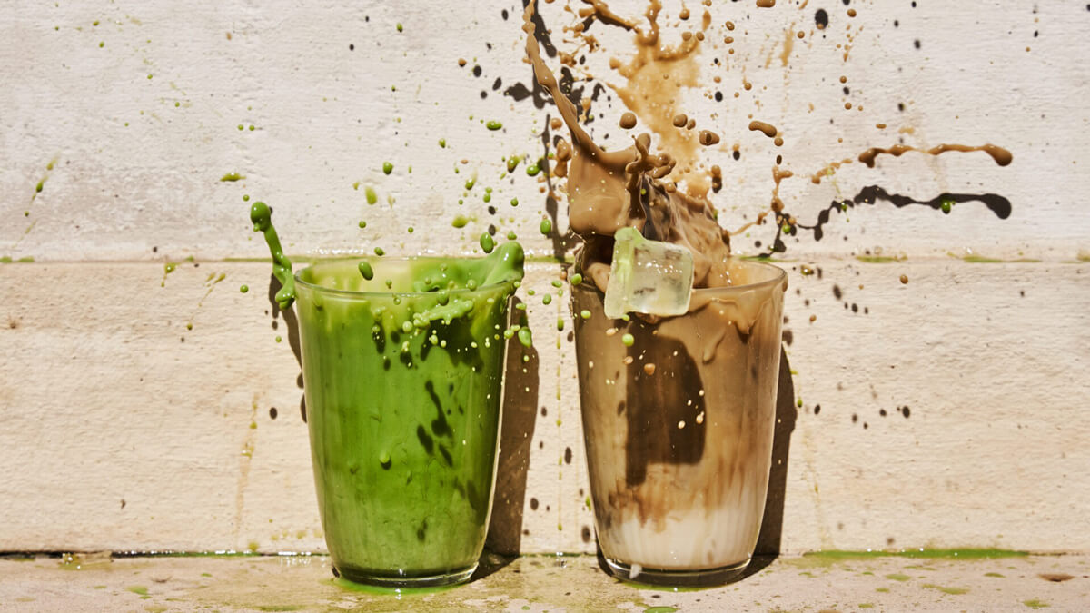 Zöld matcha és kávés-tejes ital fröccsenése két pohárban