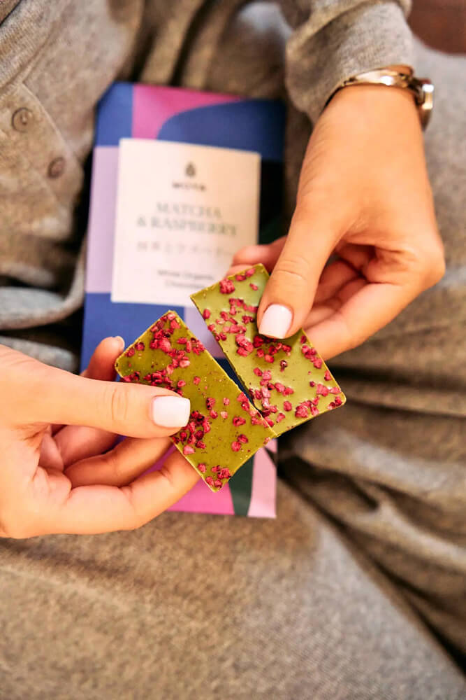 Moya Matcha Fehércsokoládé Málnával – részlet Moya Matcha Fehércsokoládé Málnával 80 g tábladarabok közelről, zöld csokoládé tetején málnadarabokkal.