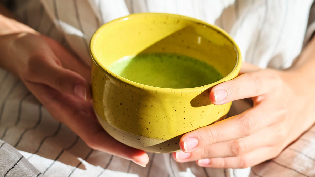 Zöld tea hatása a vérnyomásra témájú hero kép, kézben tartott sárga tál zöld teával