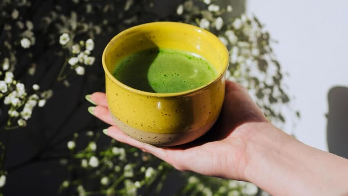 Zöld tea fogyás témájú cikkhez kézben tartott sárga matcha tál zöld teával
