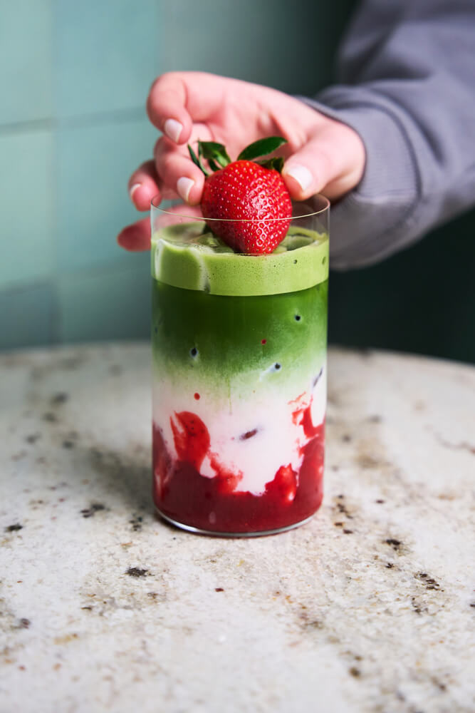 Kéz friss epret tesz a habos jeges epres matcha latte tetejére