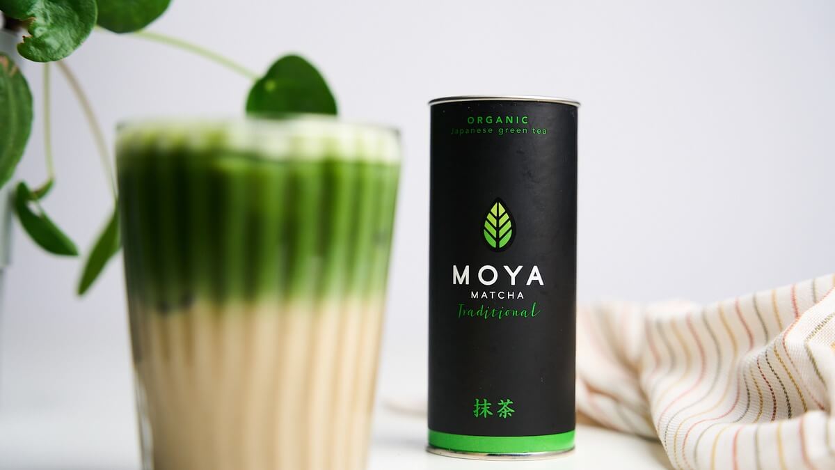 Banana bread matcha rétegezve Banana bread matcha jeges latte magas pohárban, mellette Moya matcha doboz