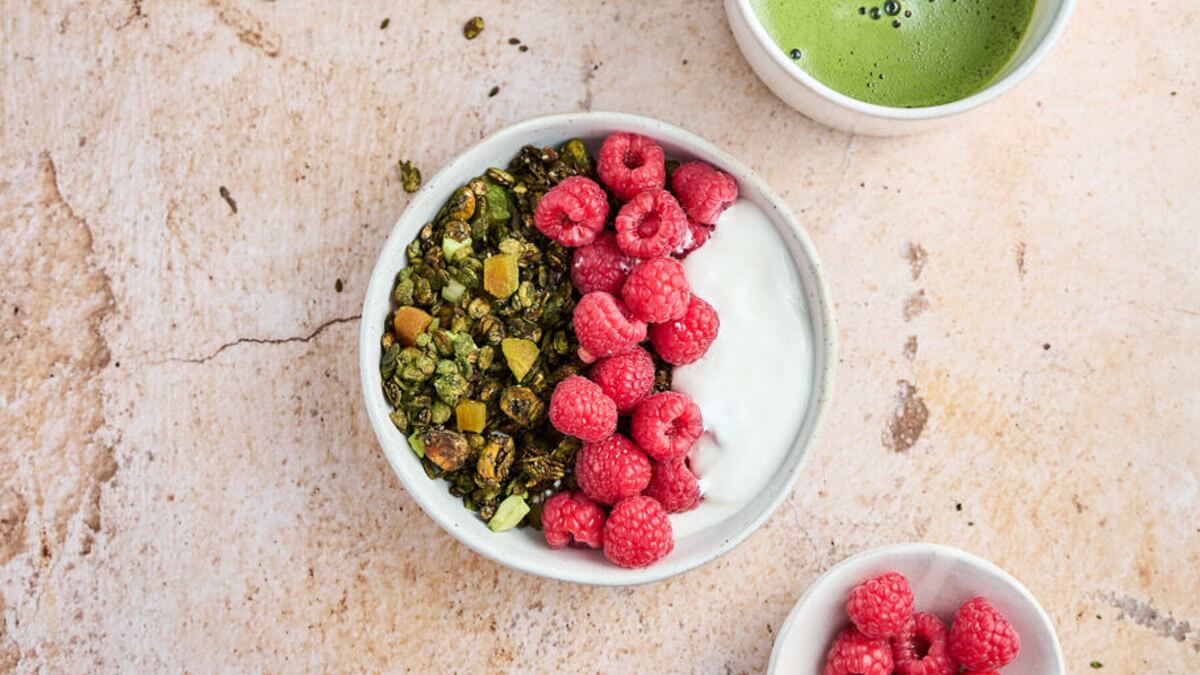 Matcha granola joghurttal és málnával Házi matcha granola tálban joghurttal és friss málnával, mellette egy csésze matcha
