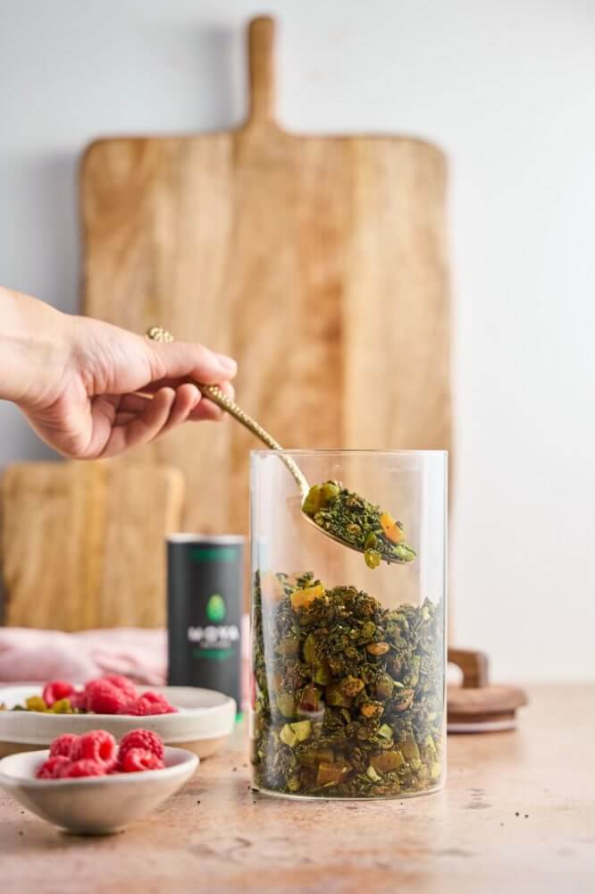Frissen sült matcha granola betöltése üvegbe, a háttérben Moya matcha doboz