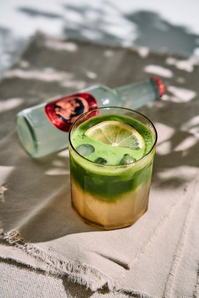 Rétegzett matcha gyömbér tonik magas pohárban jéggel és citromkarikával, felül élénkzöld matcha réteggel