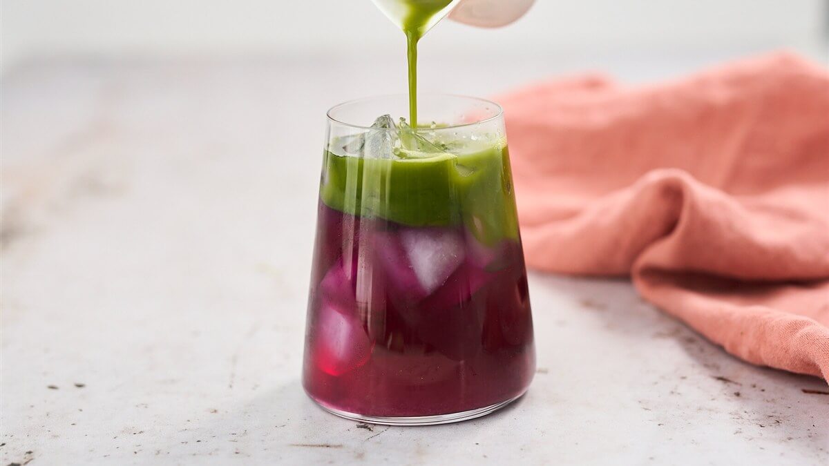 Matcha limonádé pillangóvirág-teával Rétegzett matcha limonádé pillangóvirág-teával magas pohárban, kék-lila-zöld átmenettel és jégkockákkal