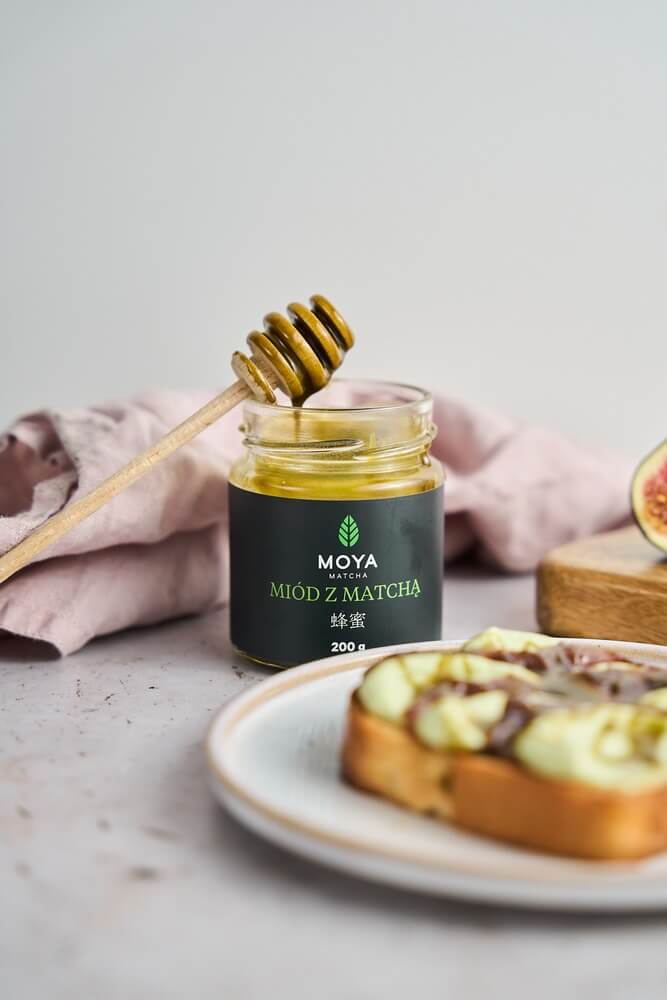 Moya matcha méz üvegben mézcsurgatóval, mögötte matchakrémes pirítós