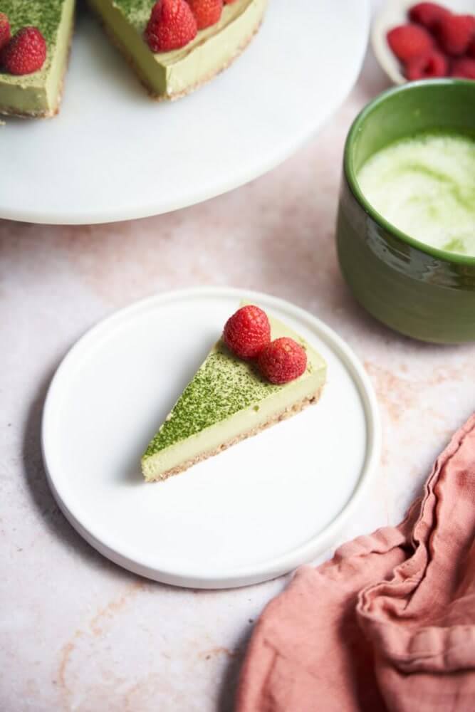 Krémes vegán matcha sajttorta szelet tányéron, friss bogyós gyümölccsel, sütés nélkül