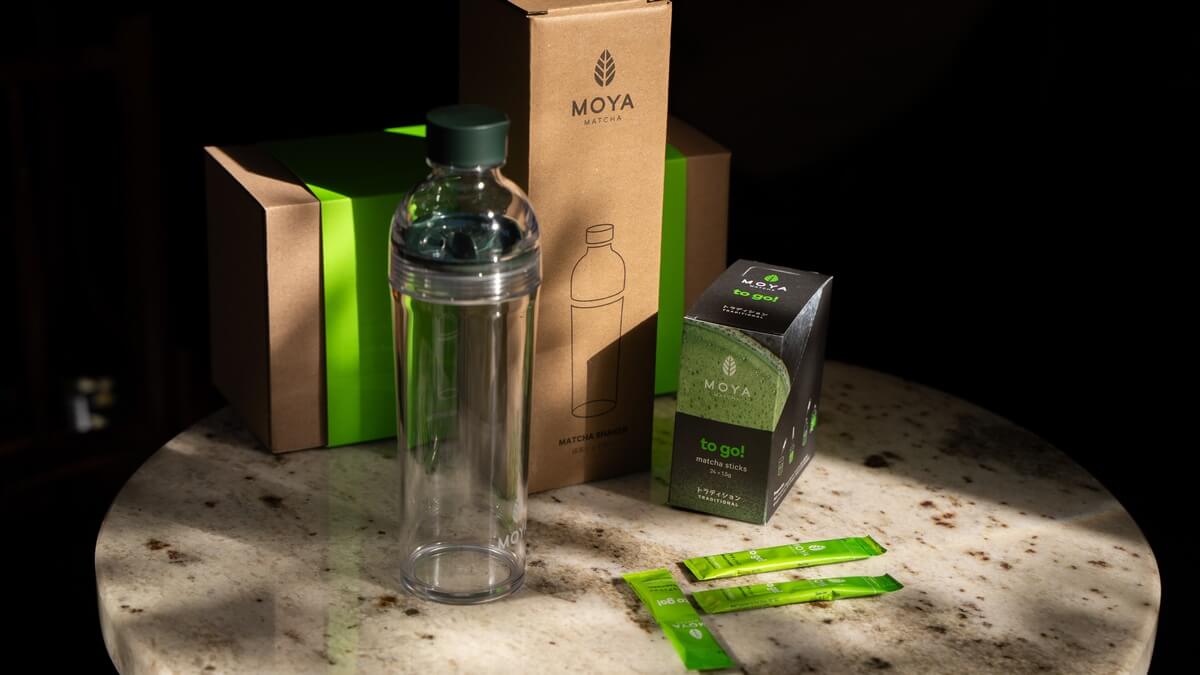 Matcha to go szett ajándékba Moya Matcha to go szett: átlátszó matcha shaker, díszdoboz és Traditional to go matcha tasakok márványasztalon.